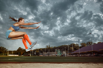 Female athlete performing a long jump during a competition at stadium. The jump, athlete, action,...