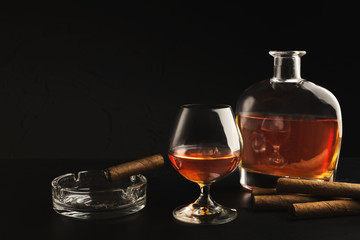 Glass with cognac, bottle and cigar on black background