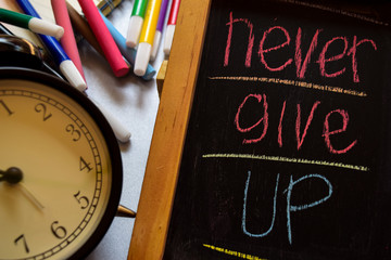 Never give up on phrase colorful handwritten on chalkboard, alarm clock with motivation and education concepts