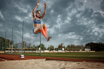 Female athlete performing a long jump during a competition at stadium. The jump, athlete, action,...