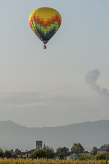 Colorful hot-air balloon flies over typical village in the Tuscan countryside in the light of the sunset