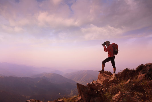 Young woman hiker taking photo on mountain peak
