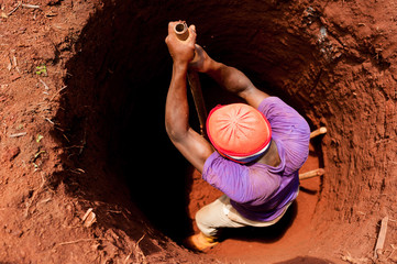 strong young boy manually digging well with shovel in african small village with red soil