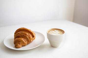 Cup of cappuccino coffee and croissant on white table