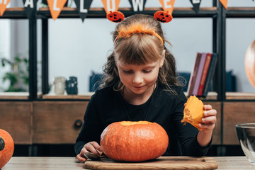 Fototapeta premium portrait of adorable child at tabletop with pumpkin for halloween at home