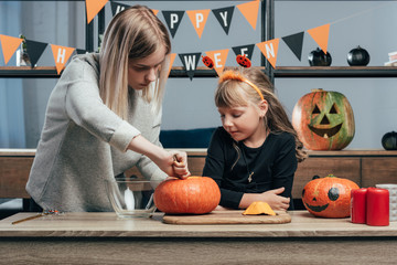 Fototapeta premium young woman helping little sister in halloween costume carving pumpkins at home