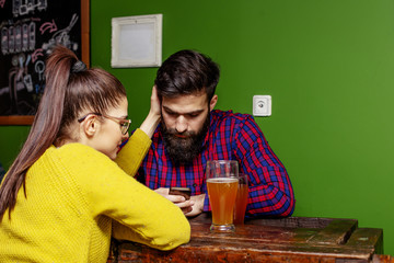 Young couple looking at mobile phone while sitting in local pub and drinking beer