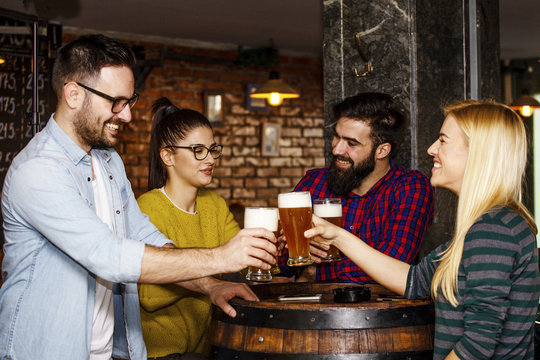 Group of four people toasting with glasses full of beer in local pub