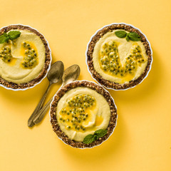 vegan raw mini tarts from nuts and dates with cashew cream from mango purée with lime juice and seeds of passion fruit. healthy alternative food on a bright yellow background
