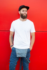Hipster handsome male model with beard wearing white blank t-shirt and a baseball cap with space for your logo