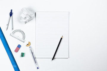A photo of stationery set: pencil, rubber, sharpener, compass, protractor, ruler and crumpled paper ball on the white background on the table . Workspace of student or office worker.