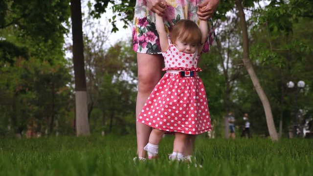 Mom turns small daughter holding hands in summer park. Girl laughs while playing with her mother outdoors Happiness of motherhood. Slow motion.