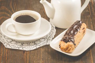 coffee cup, teapot and eclairs on a wooden background/breakfast with coffee cup, teapot and eclairs on a wooden background.