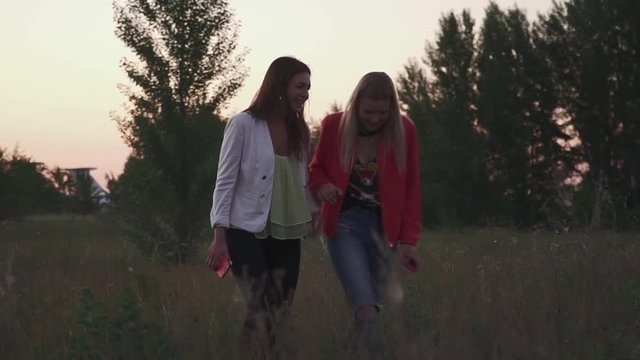 Two girls walk in the fild on sunset