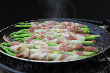 Raw bacon wrapped green asparagus in frying pan on dark background