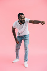 young african american man laughing and pointing away on pink background