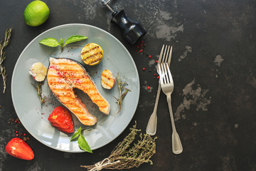 Grilled salmon steak served on a gray plate, black concrete background. Top view,flat lay. Copy space