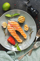 Grilled salmon steak served on a gray plate, black concrete background. Top view,flat lay.