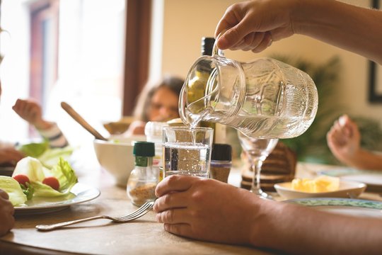 Man serving water in glass on dining table