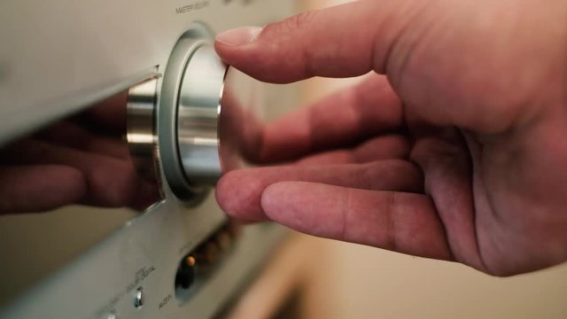 Man's hand turning a dial to increase and decrease volume on hifi stereo, close up shot