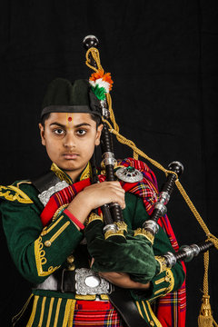 A portrait of an Indian American Scottish bagpiper looking at camera in full Scottish regalia, including kilt and sporrans
