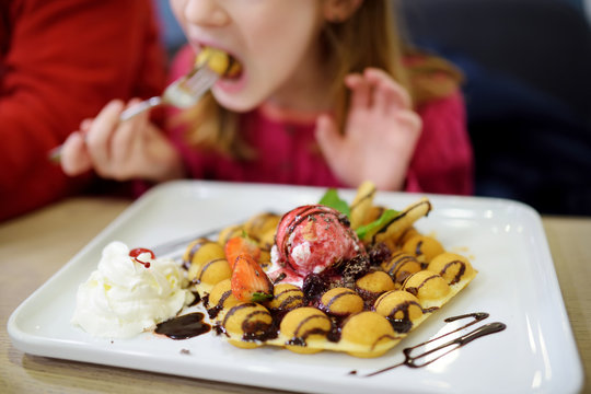 Adorable little girl eating bubble waffle with fruits, chocolate and marshmallows. Children eating sweets.