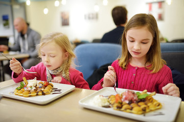 Adorable little sisters eating bubble waffle with fruits, chocolate and marshmallows. Children having sweets.