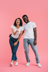 laughing african american woman pointing at camera with boyfriend standing near on pink background