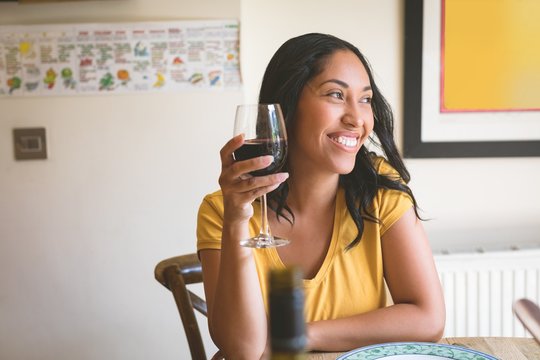 Woman having red wine on dining table at home