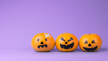 Three Fresh Oranges with Halloween Pumpkins painted face.  Easy DIY decoration for Halloween festival on violet background