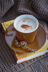 Autumn mood. Coffee cappuccino with cinnamon, book and knitted pullover on a brown background