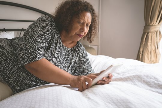 Senior woman using digital tablet on bed in bedroom