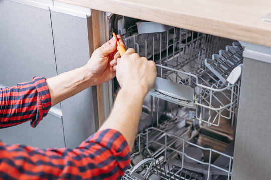 man repairing dishwasher. Male hand with screwdriver installs kitchen appliances