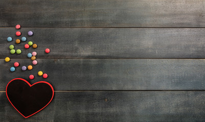 Heart shaped blackboard and candies on wooden background, top view and copy space.
