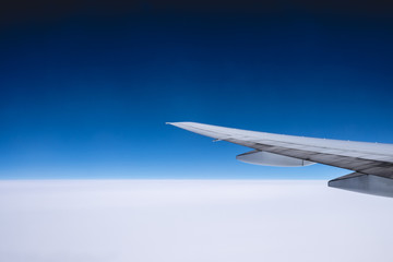 Plane wing flying over the clouds and the blue sky