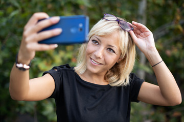 Beautiful blonde girl with eyeglasses on top of her head playing with her smartphone making selfie