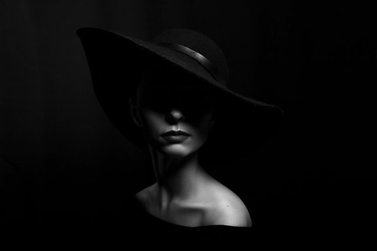 portrait of a woman in a black hat on a black background black and white photo
