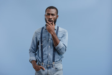 shocked african american man closing mouth by hand isolated on blue background