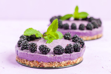 Raw blackberry dessert decorated with fresh ripe forest berries and green mint leaves on pastel violet background.