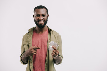 smiling handsome african american man pointing on condoms isolated on white