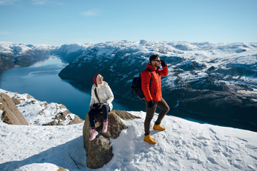 Young man and woman standing on the Pulpit Rock, Preikestolen. Scenic landscape of fjord between...