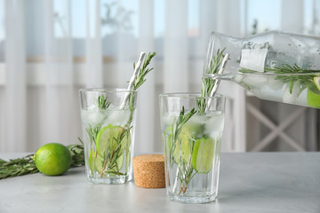 Pouring tasty refreshing cocktail with rosemary and lime into glass on table © New Africa