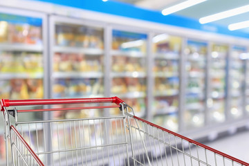 Supermarket refrigerators freezer aisle blur defocused background with empty red shopping cart