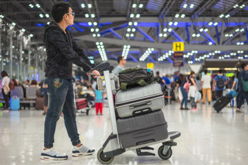 Young asian man holding cart of suitcase or baggage with airport luggage trolley in the...
