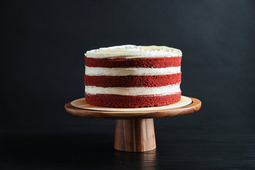 Delicious homemade red velvet cake on wooden stand against black background