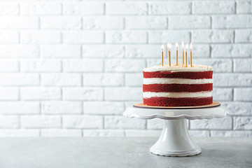 Delicious homemade red velvet cake with candles on table against brick wall. Space for text