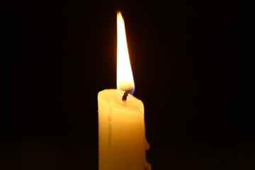 big wax flaming candle with vivid fire against heavy black background.