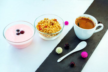Cup of freshly brewed coffee on black stone tray with berry yoghurt and granola in a glass bowls.  Served breakfast.