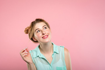 smiling pretty young girl looking up and right at a virtual object or text speech bubble. empty space for advertising. portrait of a cute blond on pink background.