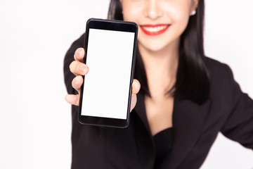 Close up of smiling business woman in black formal suit holding and showing mobile phone with empty copy space screen in white isolated background.